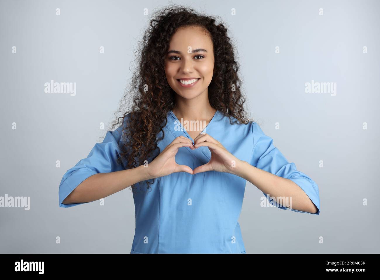 Happy young African-American doctor making heart with hands on light ...