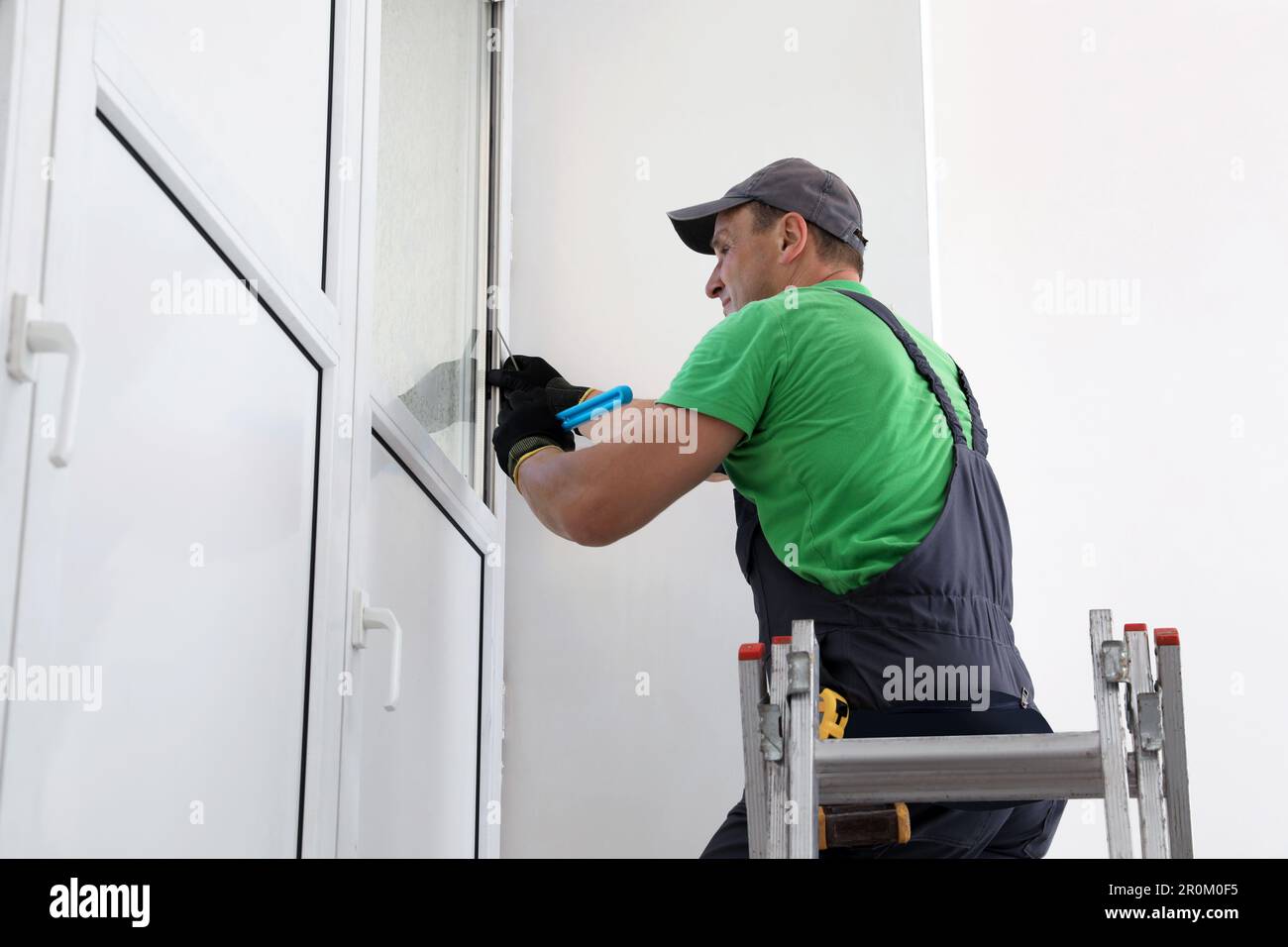 Worker on folding ladder installing window indoors Stock Photo