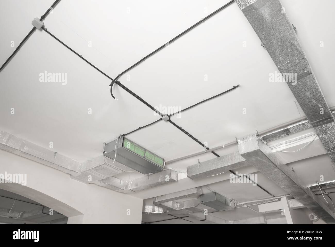 Conduits with cables and ventilation system on white ceiling, low angle