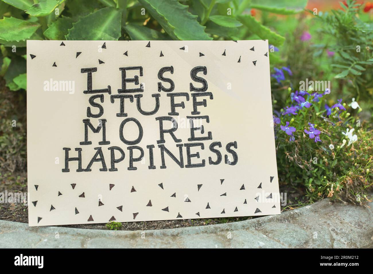 Card with phrase Less Stuff More Happiness on stone planter outdoors Stock Photo
