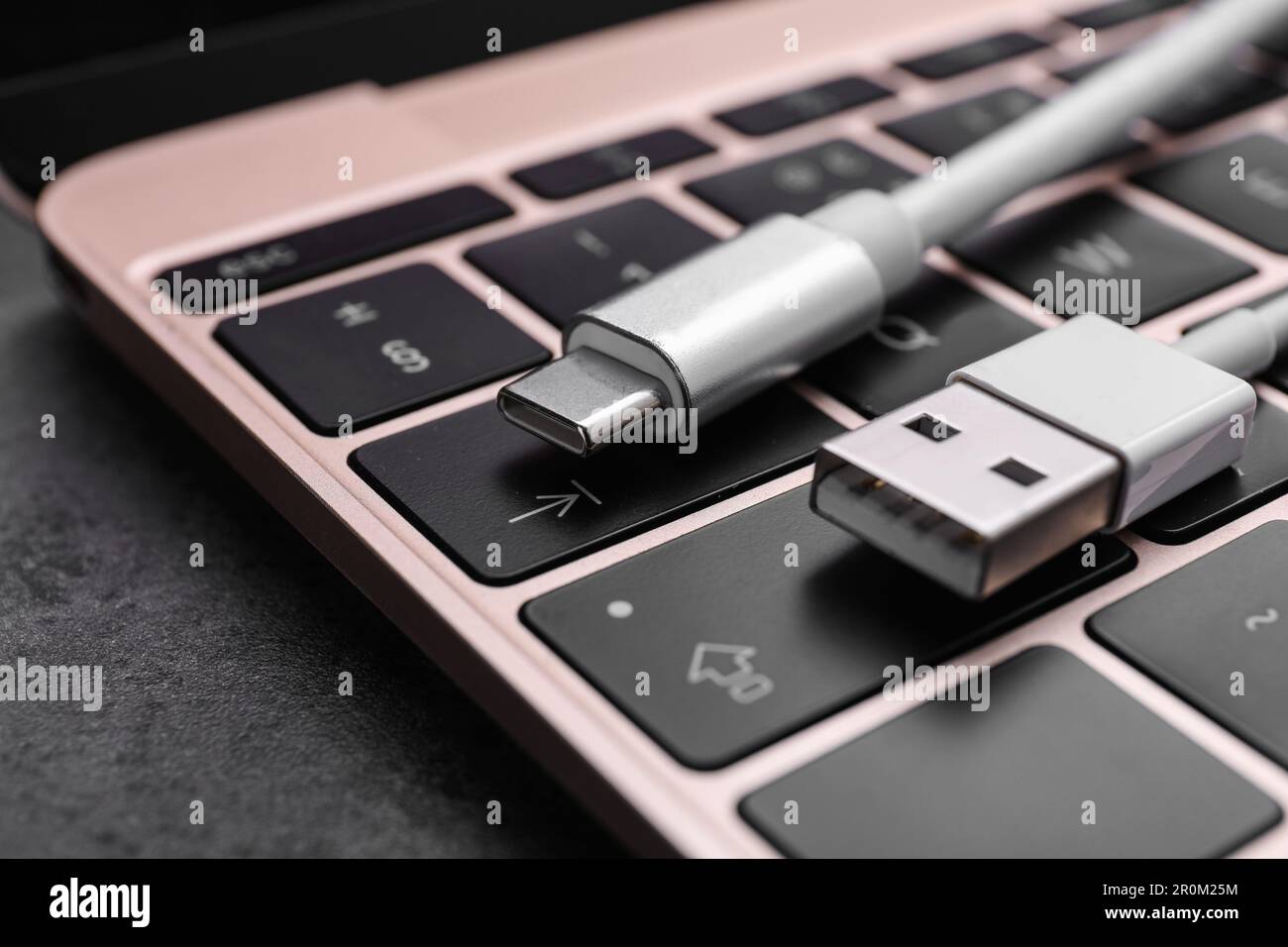 USB cable with type C connector and laptop on dark table, closeup Stock Photo