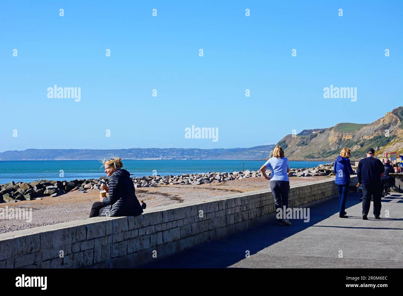 Tourists on the promenade with views of the beach and Jurassic Coast, West Bay, Dorset, UK, Europe. Stock Photo