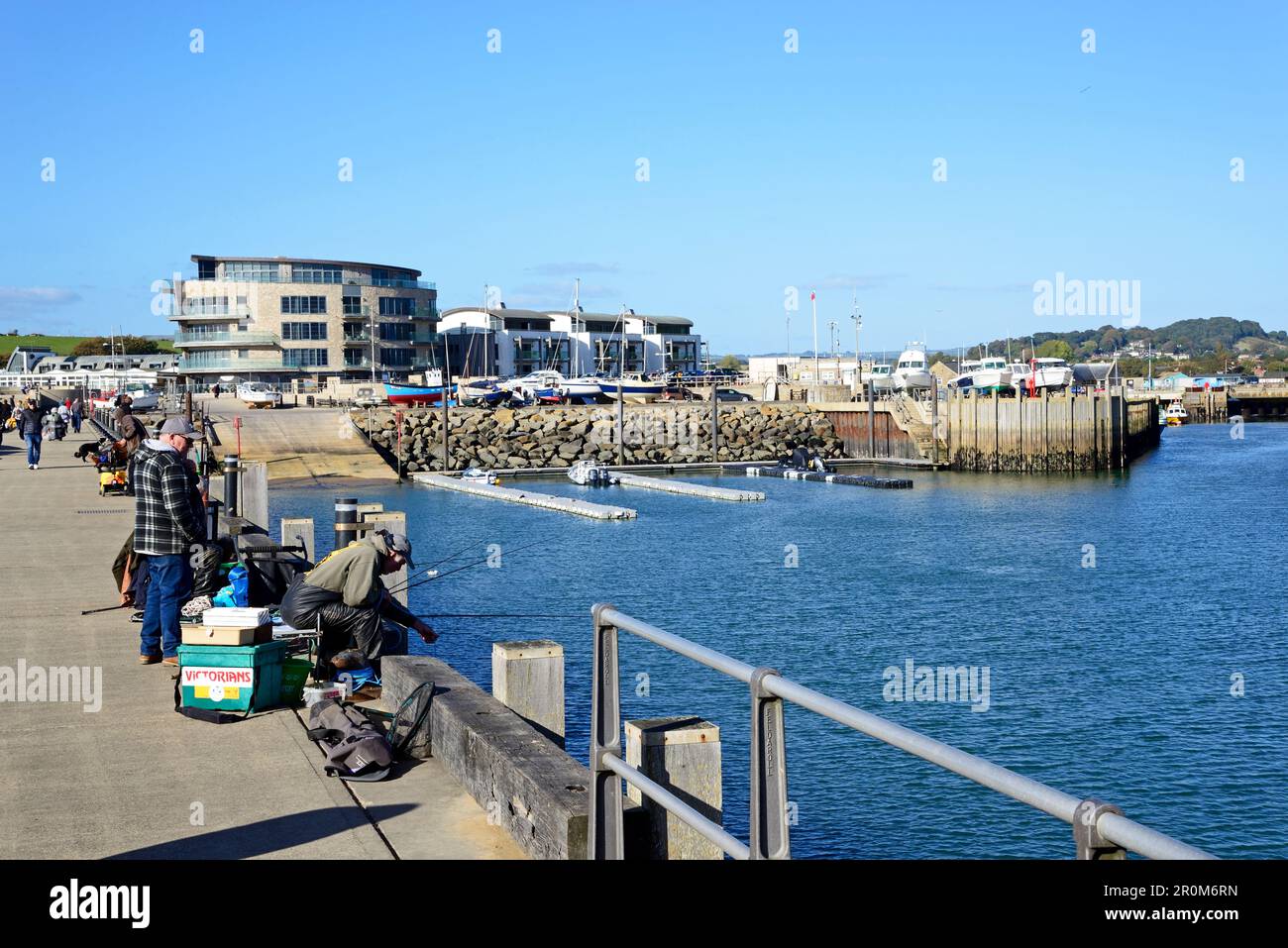 Men fishing from the harbour pier with town buildings to the rear, West Bay, Dorset, UK, Europe. Stock Photo