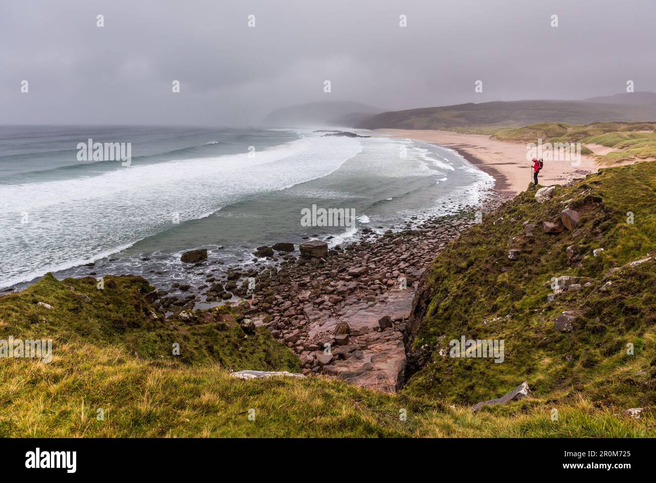 A female wanderer stands on a hill on the beach of Sandwood Bay, Highlands, Scotland, United Kingdom Stock Photo