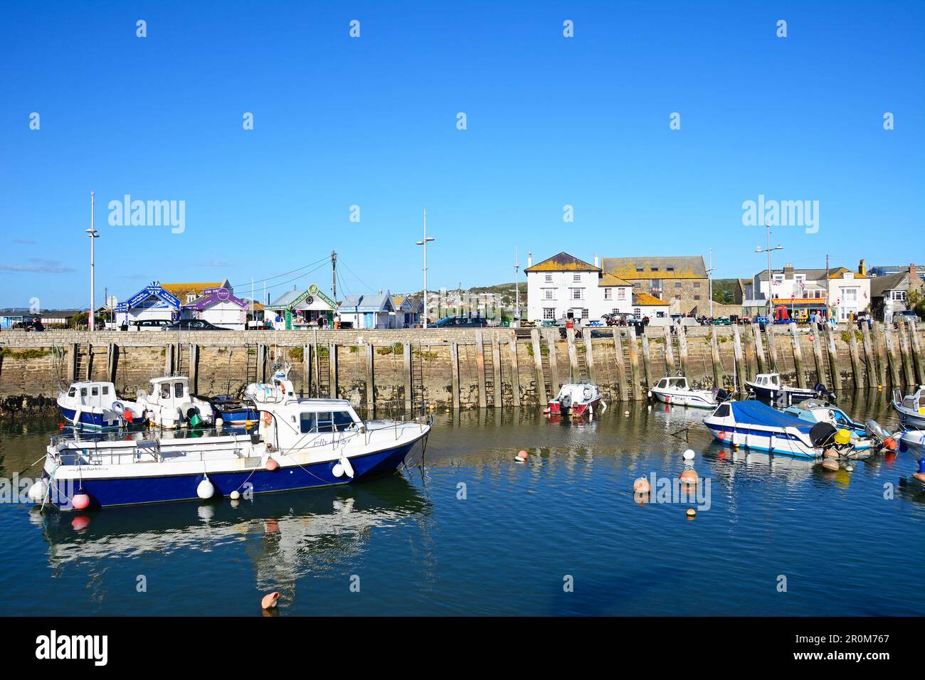 View of traditional fishing boats moored in the harbour at low tide with town buildings to the rear, West Bay, Dorset, UK. Stock Photo