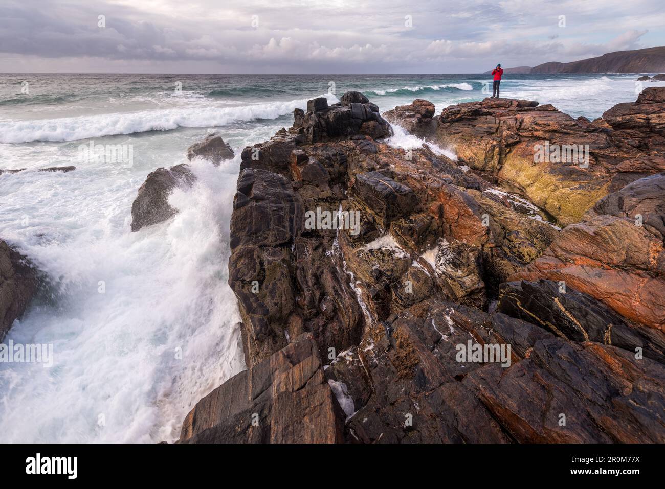 A man stands on a rock in front of the surf at Sandwood Bay, Highlands, Scotland, UK Stock Photo