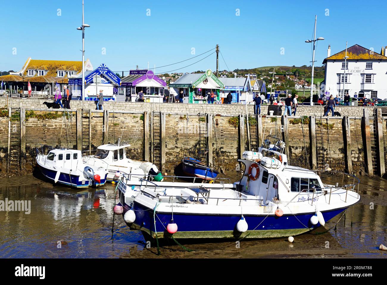 View of traditional fishing boats moored in the harbour at low tide with town buildings to the rear, West Bay, Dorset, UK. Stock Photo