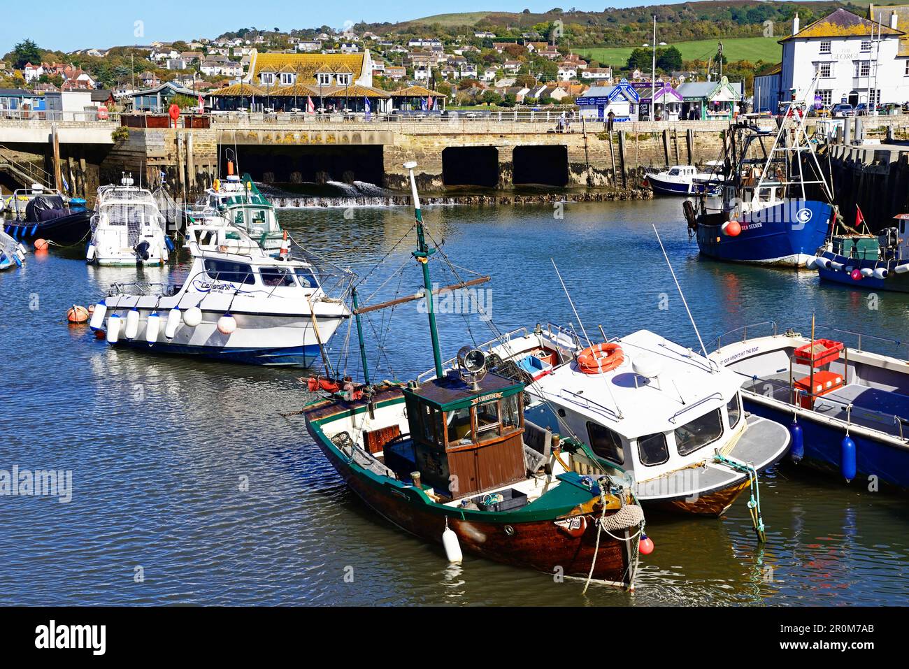 View of traditional fishing boats moored in the harbour at low tide with the town and countryside to the rear, West Bay, Dorset, UK. Stock Photo