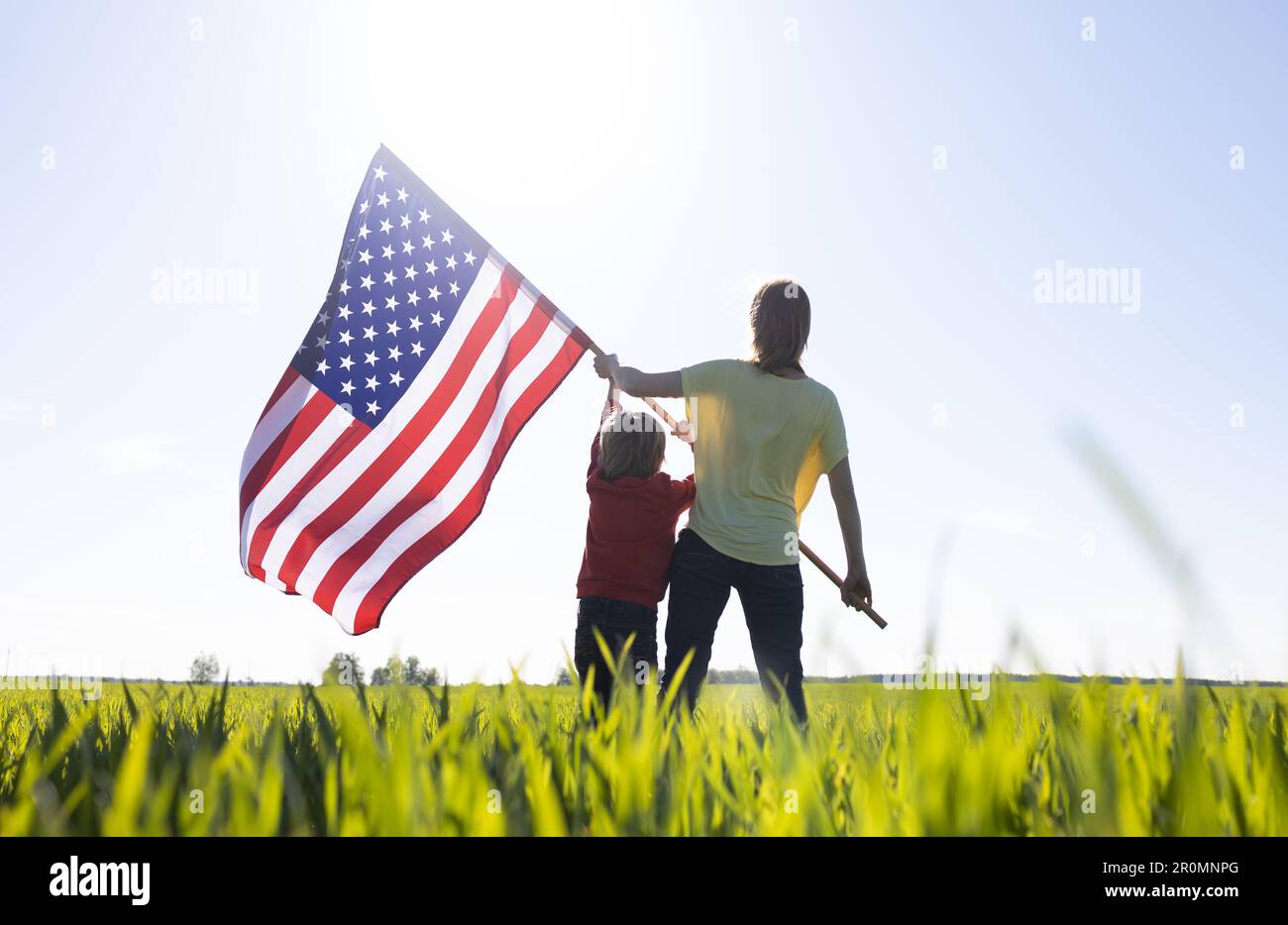 woman and child, mother son stand with their backs proudly holding an American flag in front of the bright sun. patriotic holiday, Independence Day. P Stock Photo