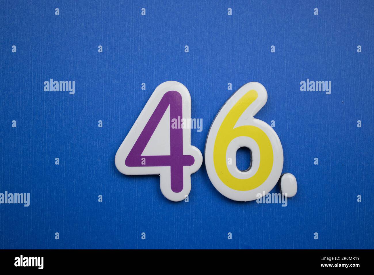 The number 46, placed on a blue background, photographed from above, colored purple and yellow. Stock Photo
