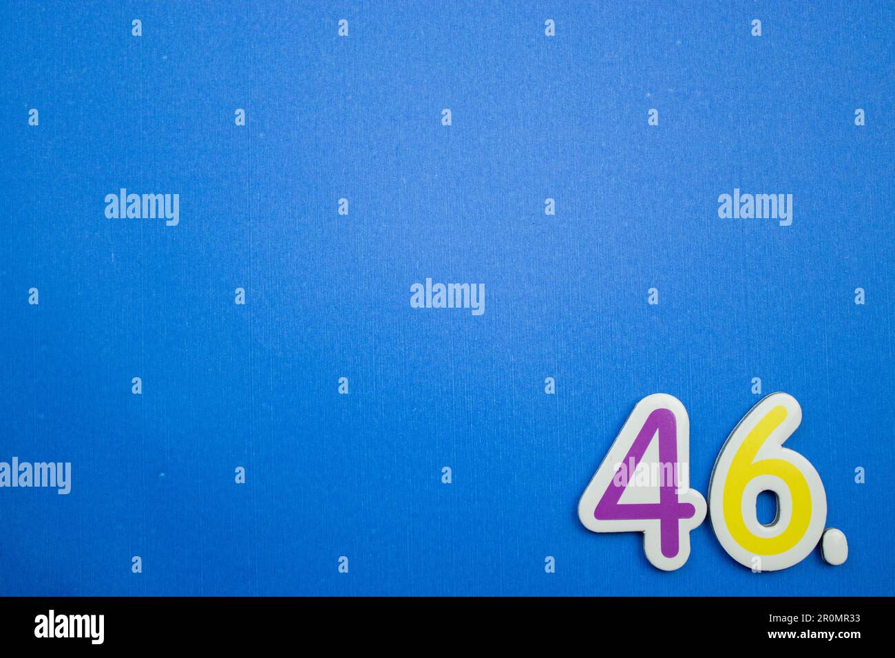 The number 46, purple and yellow, photographed from above, placed on the edge of a blue background. Stock Photo