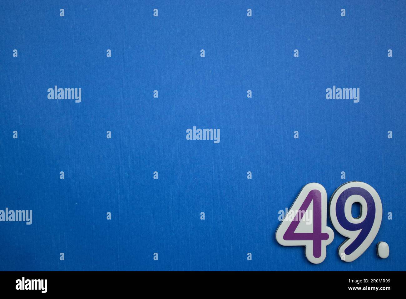 The number 49, placed on the edge of a blue background, photographed from above, colored purple and dark blue. Stock Photo