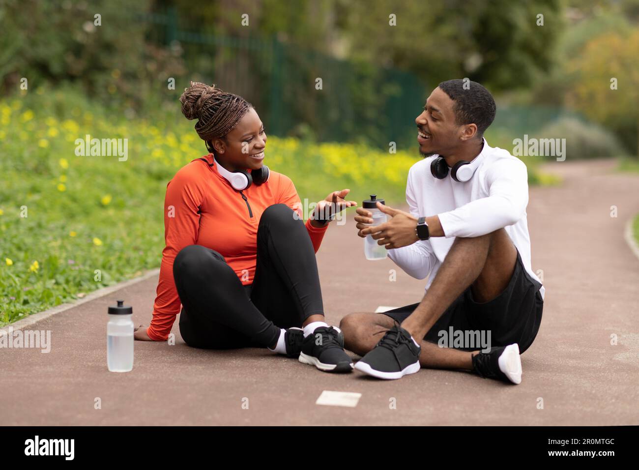 Smiling young african american husband and wife sitting on road ...