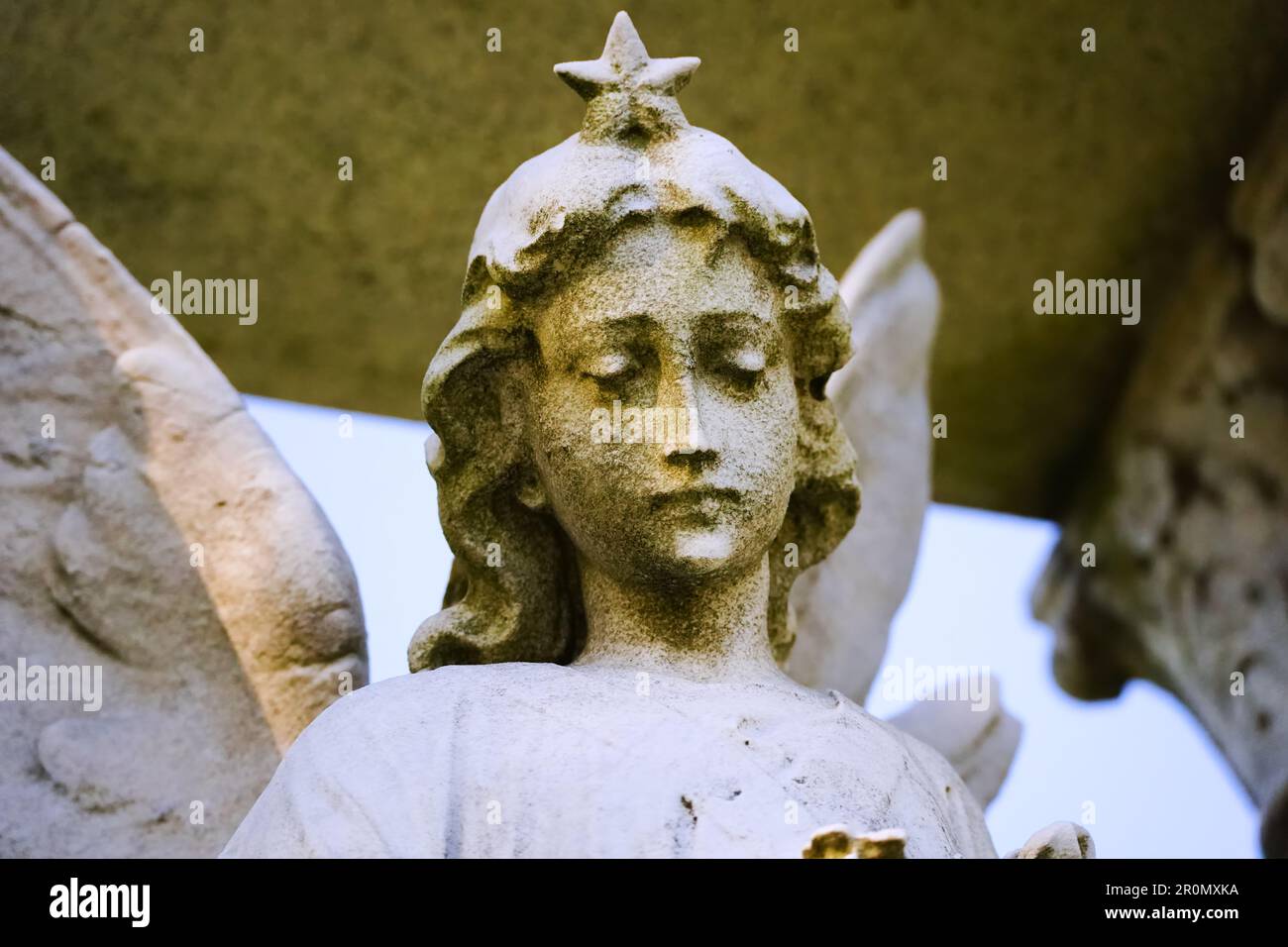 Weathered and mossy beautiful 1920s art deco style angel statue face close up with star in New York cemetery Stock Photo