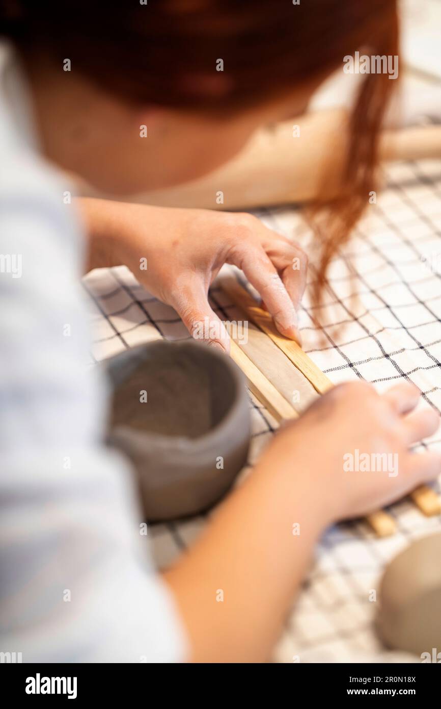 Anonymous female artisan using wooden sticks to make straight clay ...