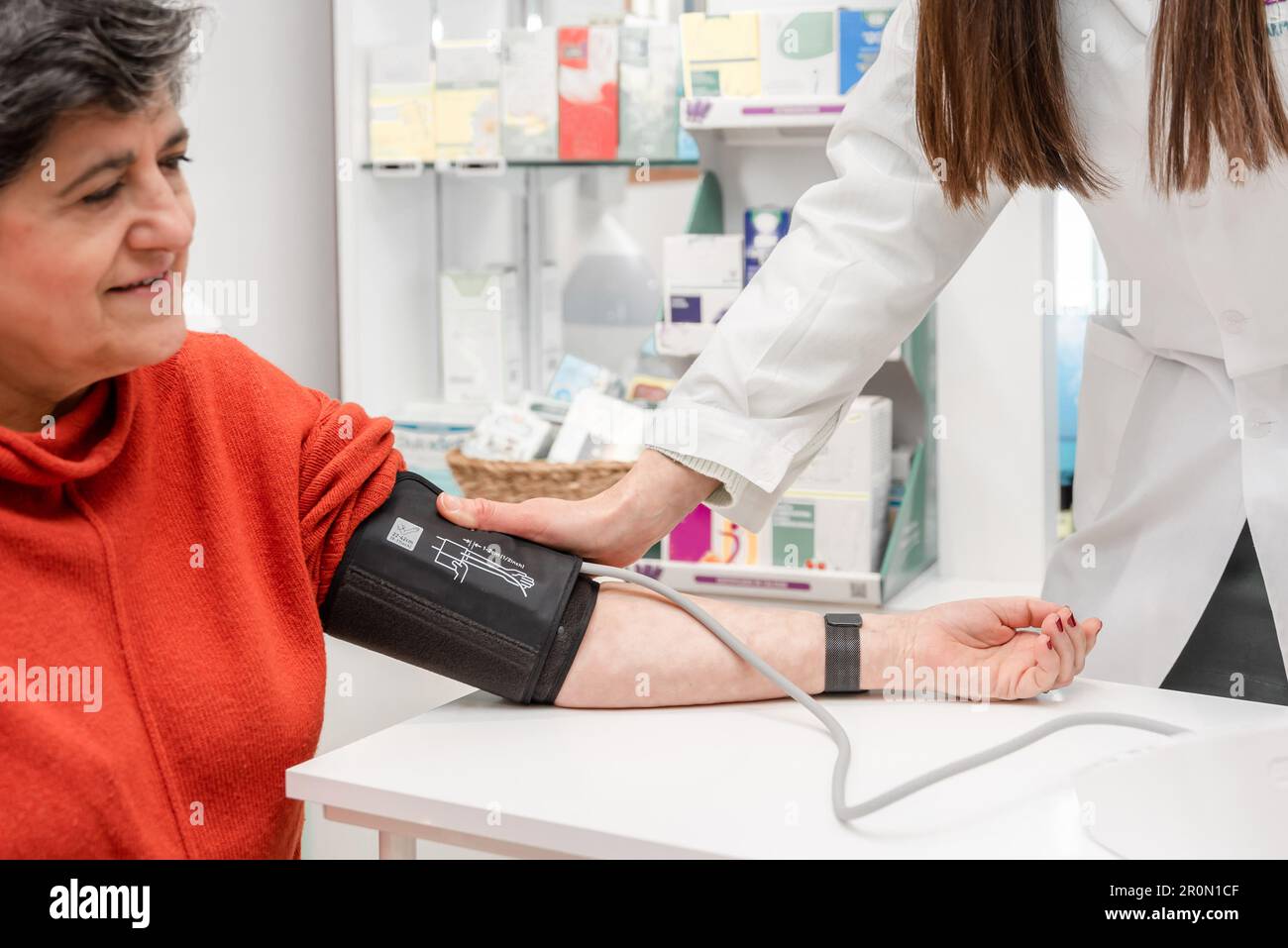 Anonymous female pharmacist in white robe using sphygmomanometer while