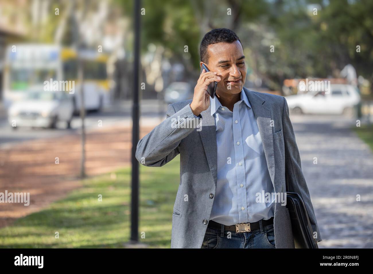 Young latin man in suit walking and talking on mobile phone. Stock Photo