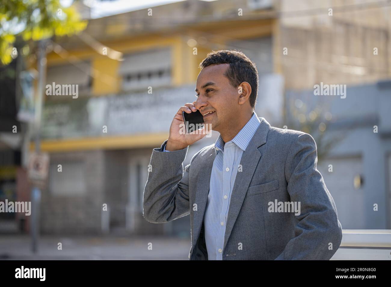 Young latin man sitting on a square bench talking on mobile phone with copy space. Stock Photo