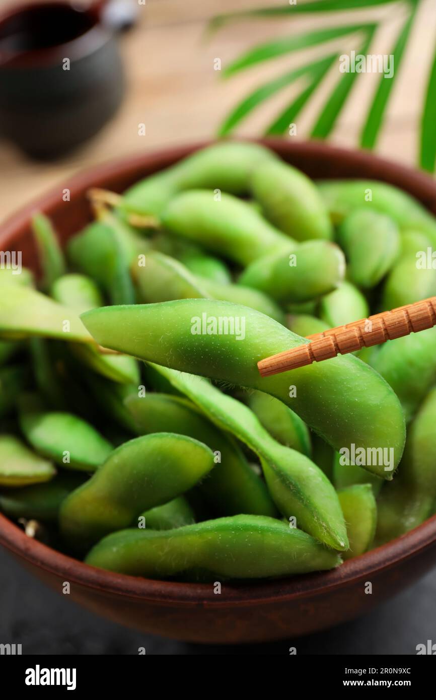 Taking edamame beans in pod from bowl with chopsticks, closeup Stock