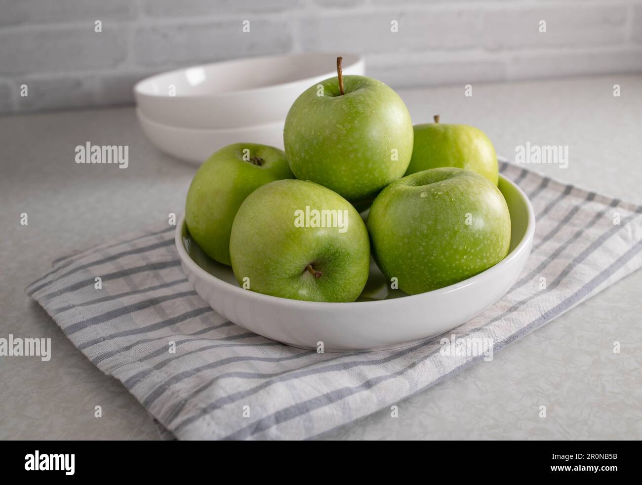 Green apples in a white bowl on kitchen table Stock Photo