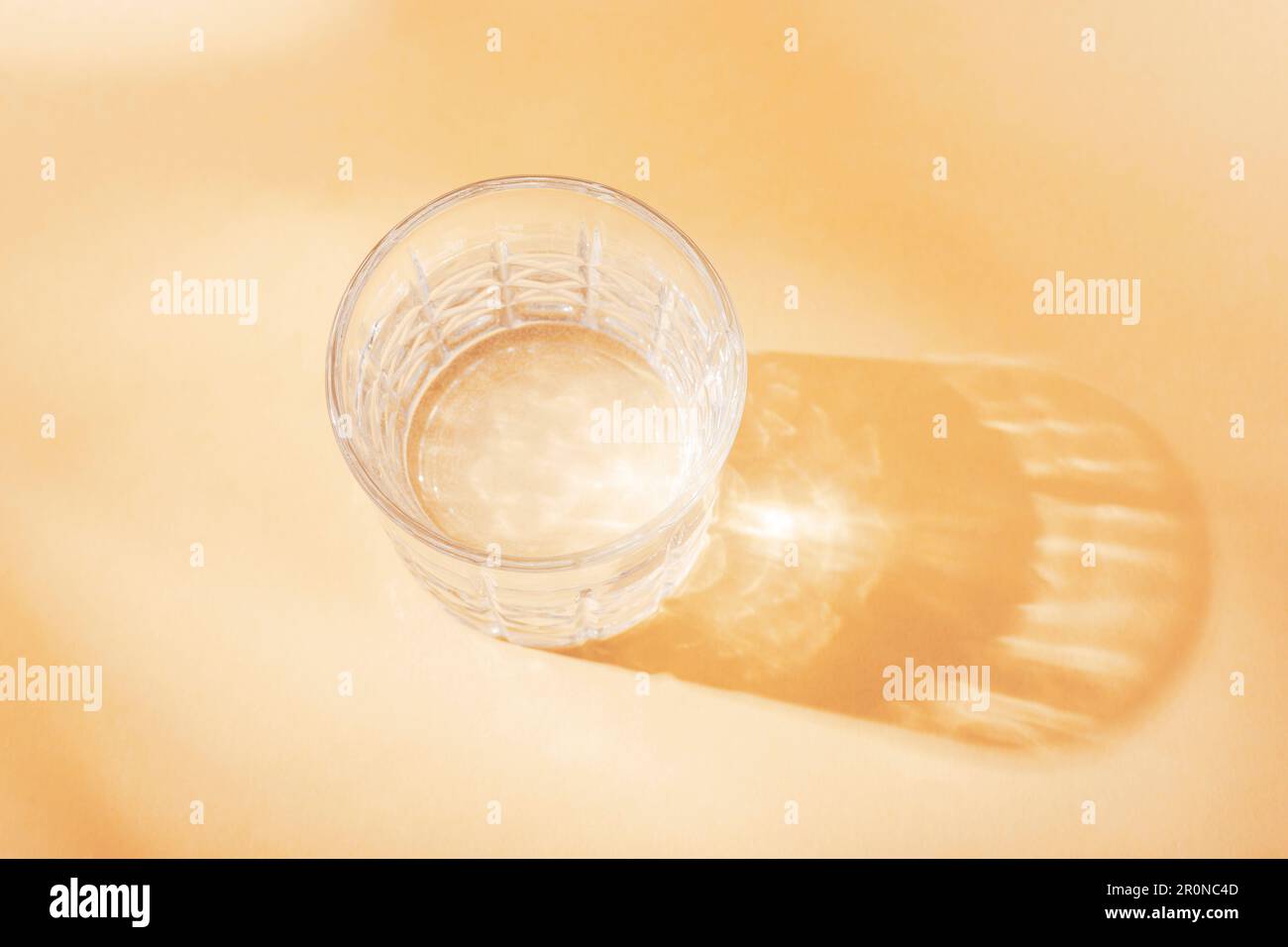 A glass with water in sunlight on neutral beige background, top view ...