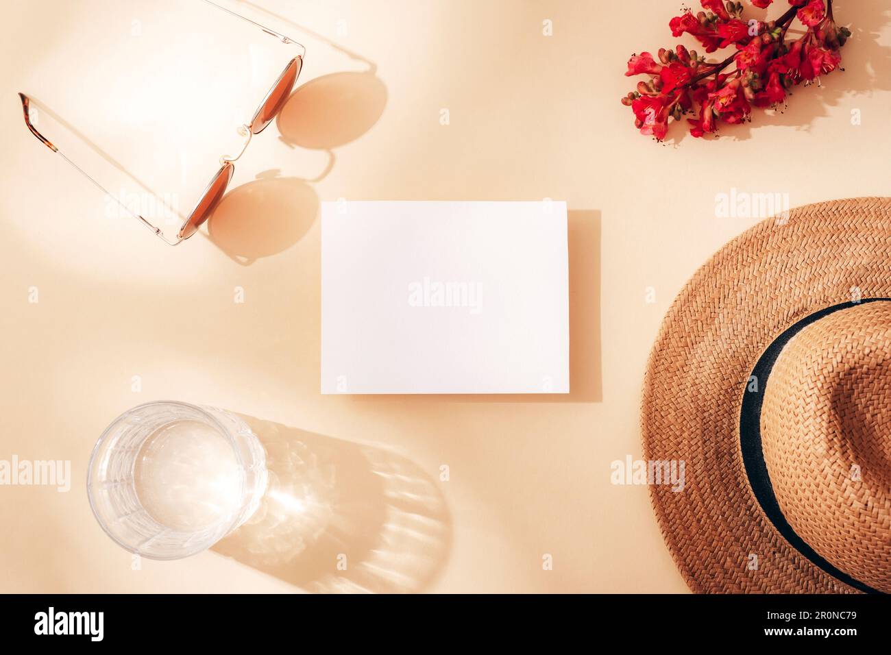 Blank card, glass of water, straw hat, sunglasses and red flower. Top view, flat lay, mockup. Stock Photo