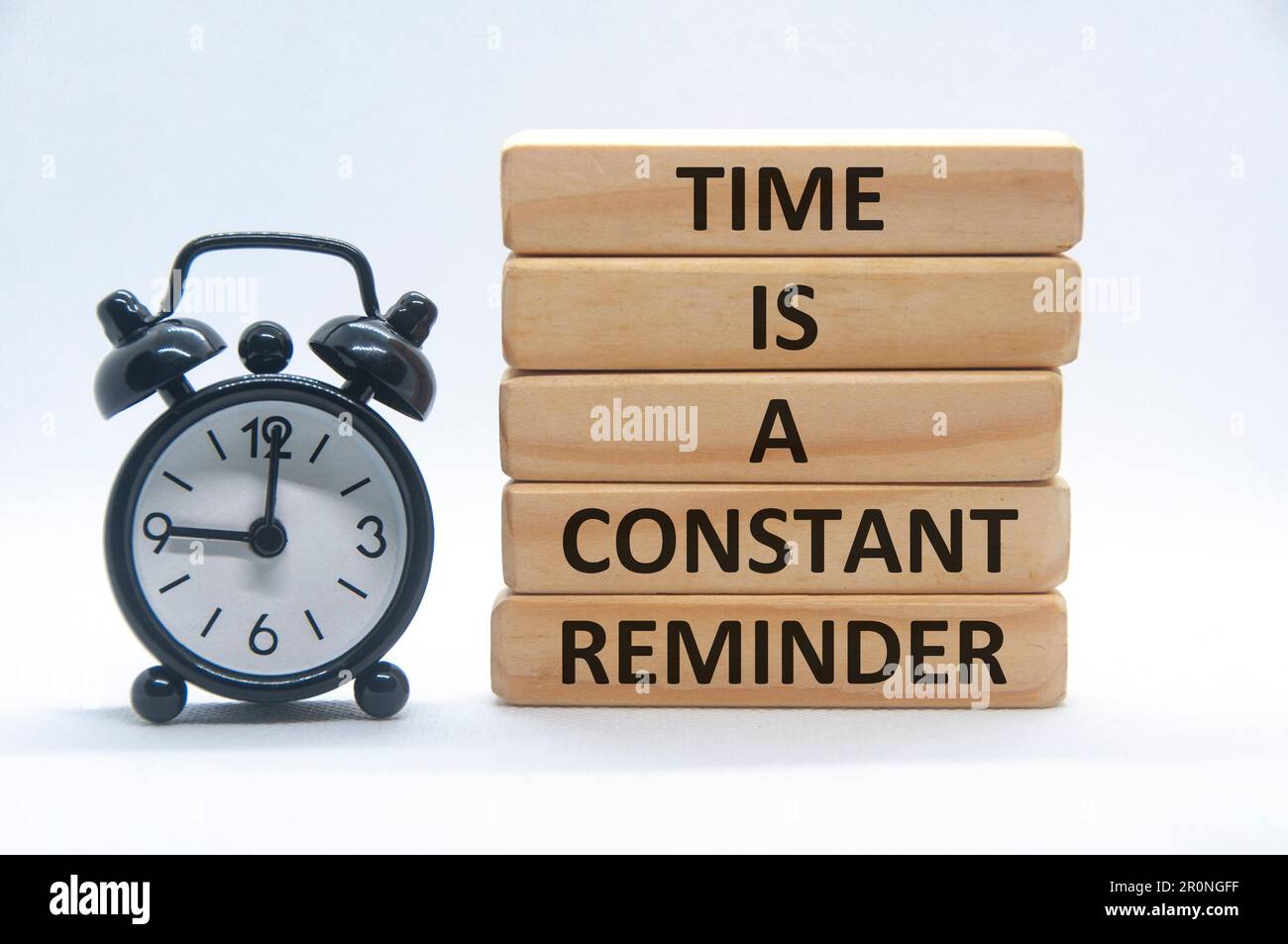 Time is a constant reminder text on wooden blocks with alarm clock on white background. Stock Photo