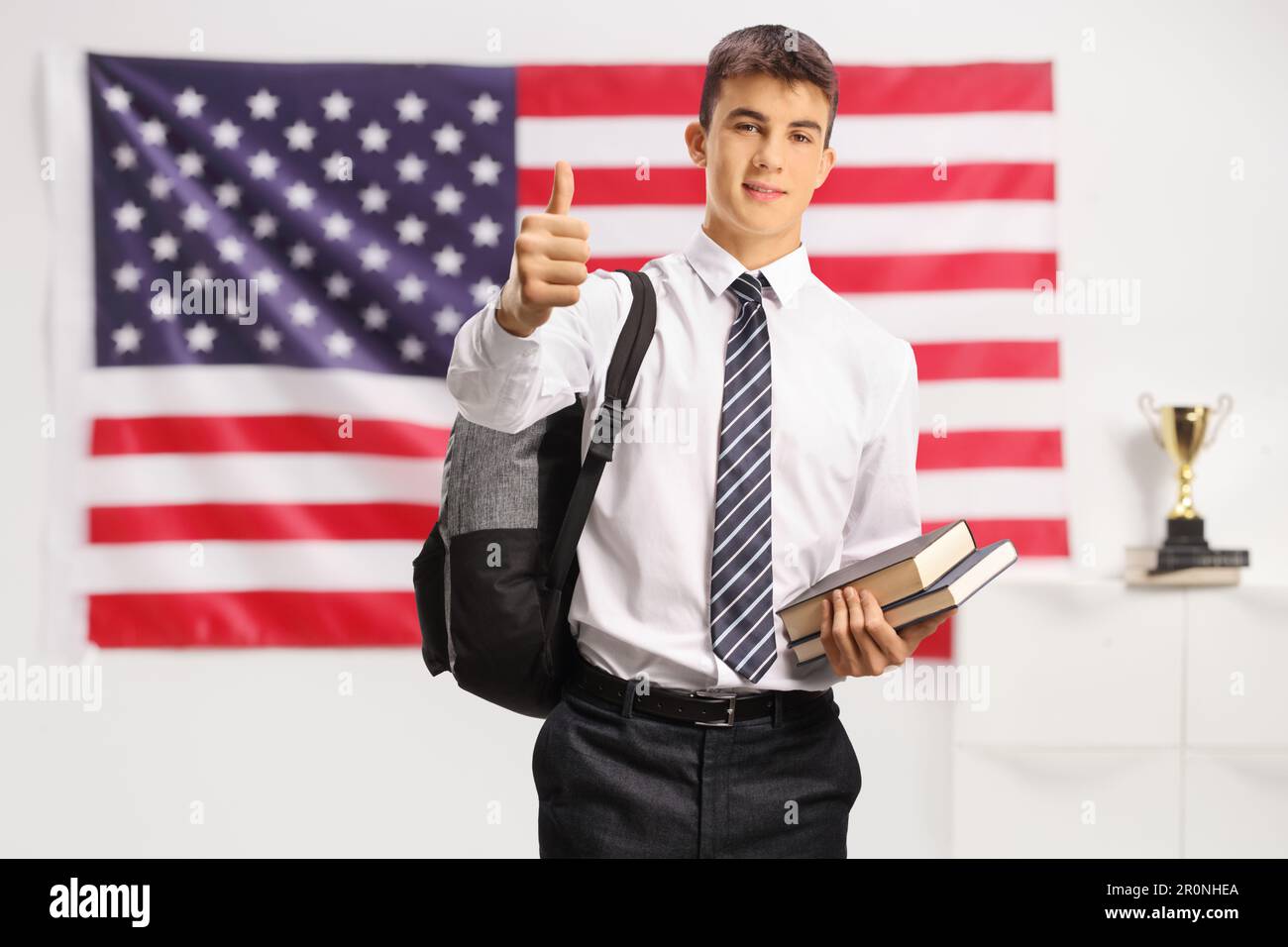 Teenage male student holding books and showing thumbs up in front of a ...