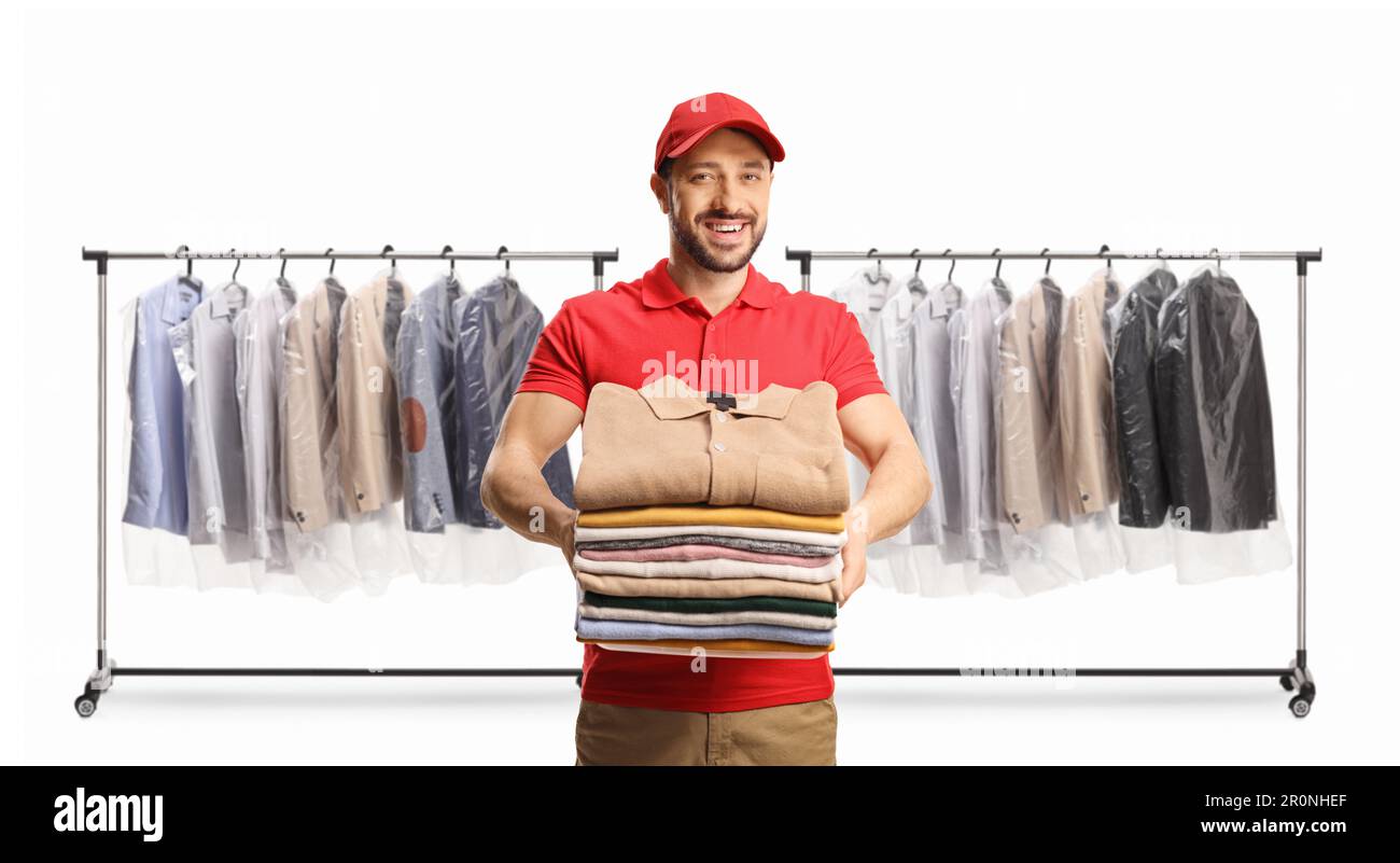Male worker holding a pile of folded clothes in front of clothing racks isolated on a white background Stock Photo