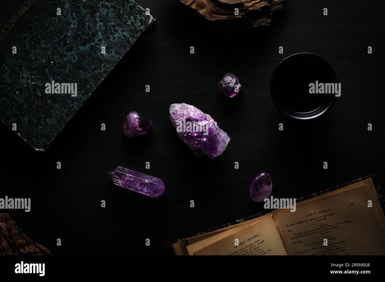 Amethyst gemstone detail on black table with french book, wood piece. Dark gothic witch top view background Stock Photo