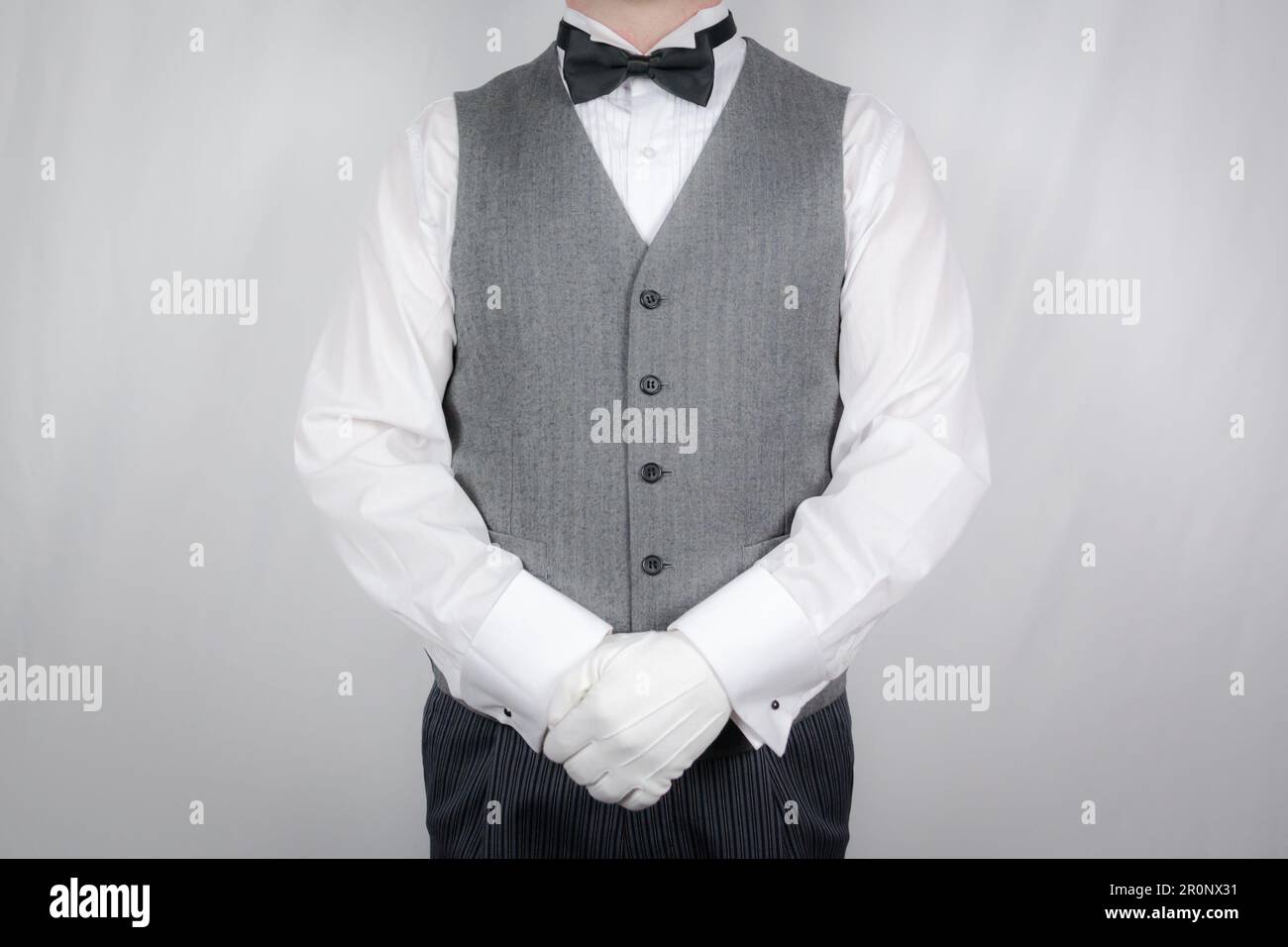 Portrait of Butler or Waiter in Gray Vest and White Gloves Standing and Respectful Attention. Service Industry and Professional Hospitality. Stock Photo