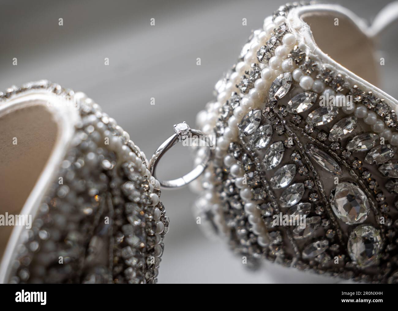 Beautiful diamond solitaire wedding engagement ring held between stunning jewel encrusted high heel shoes Stock Photo