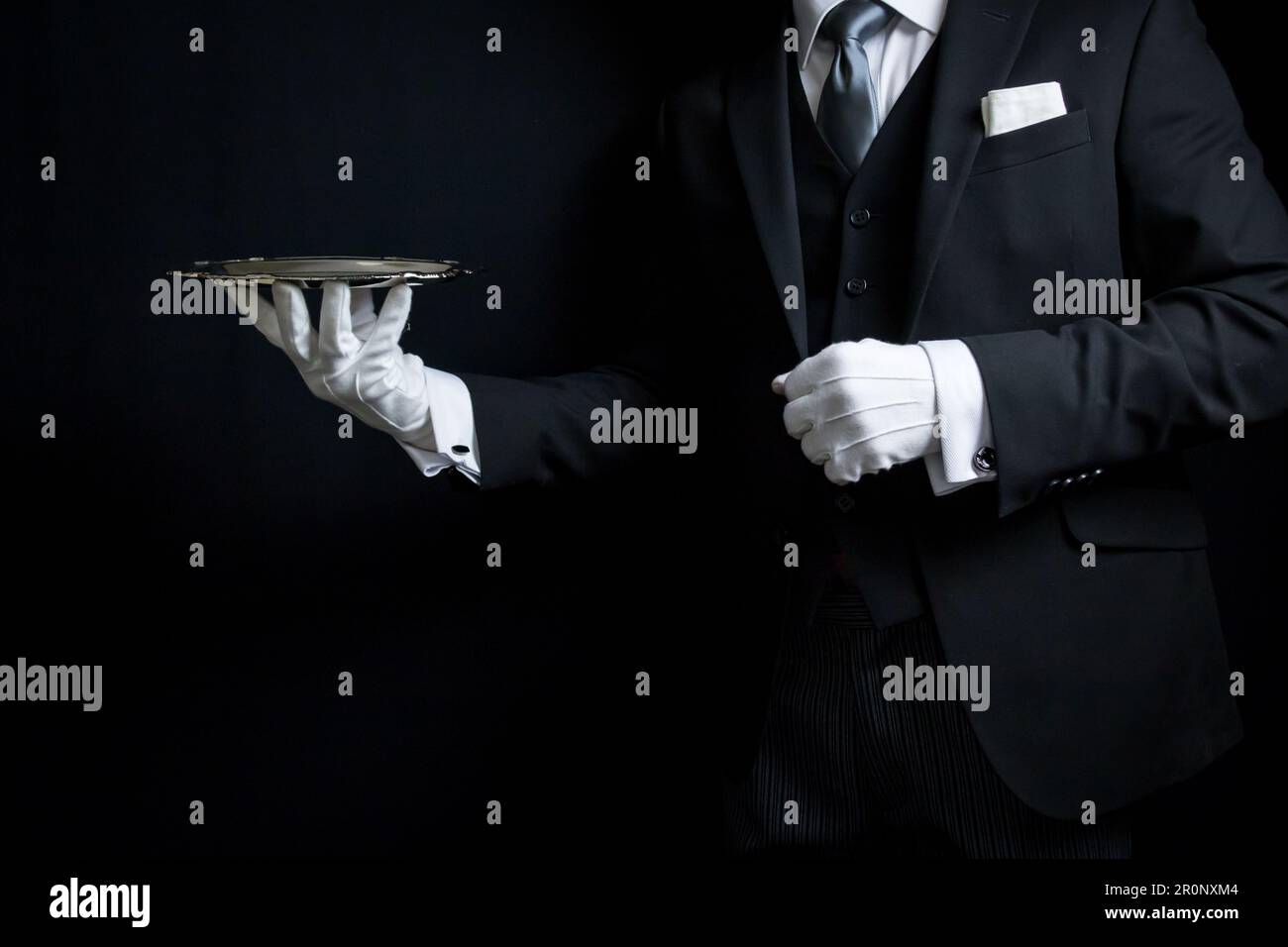 Portrait of Elegant Butler or Concierge in Dark Suit and White Gloves Holding Silver Serving Tray. Stock Photo