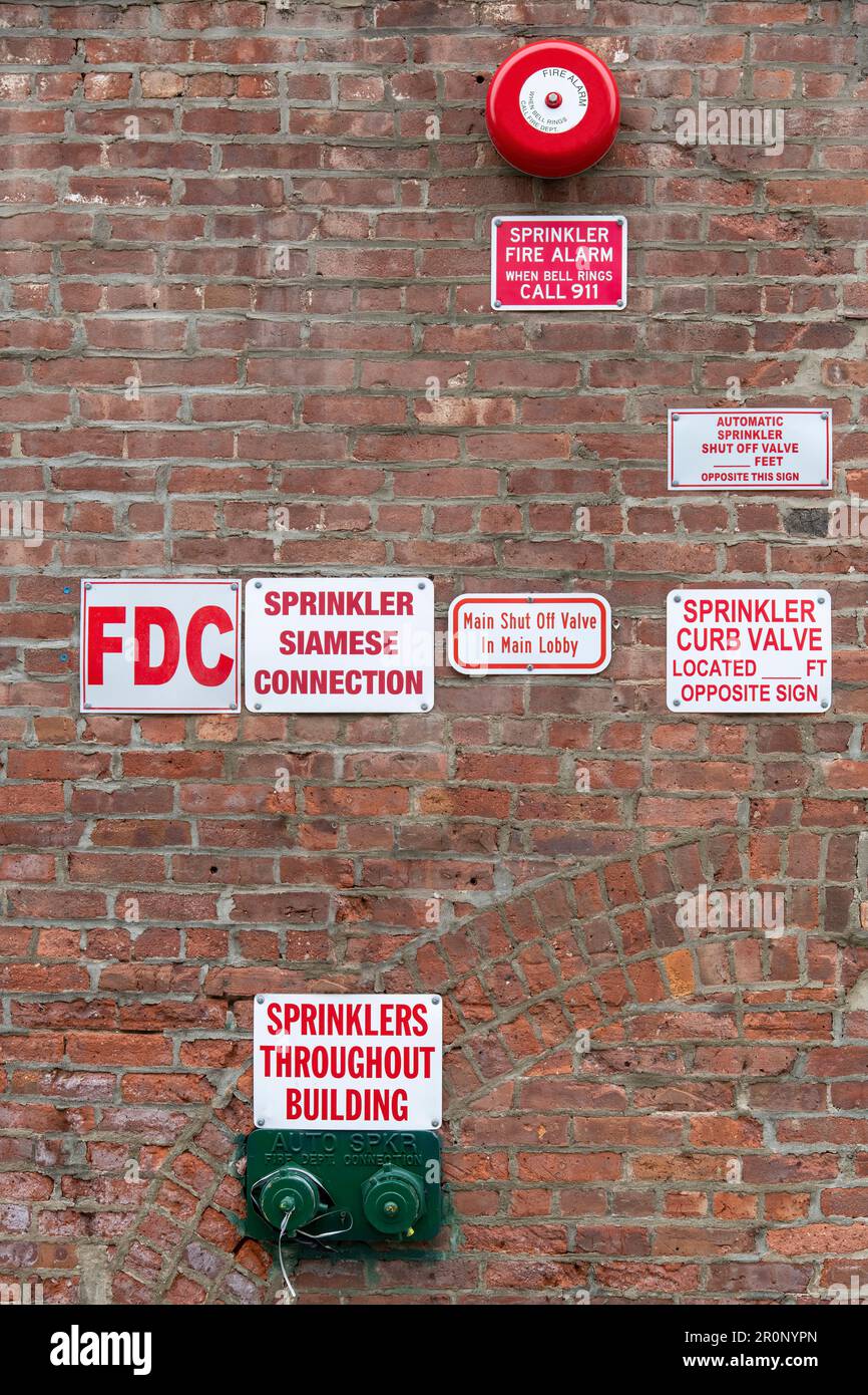 Close up view of a red brick wall with scattered on facade large number of signs to inform about sprinklers, fire, connections, shut off valve Stock Photo