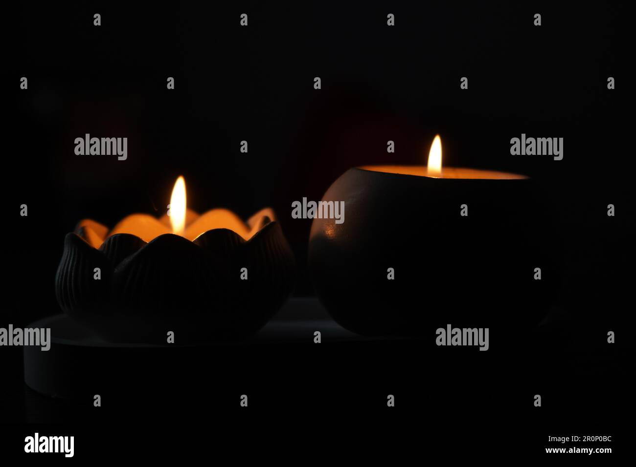 A set of lit white candles flickering in the dark on a black background ...