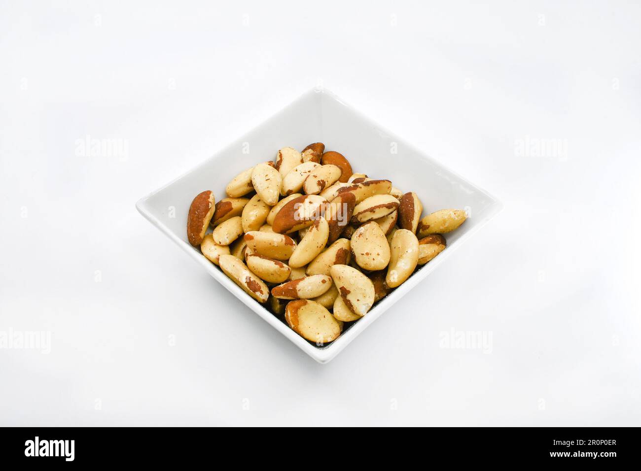 White square shaped dish with brazil nuts isolated on a plain white background. Copy space. Stock Photo