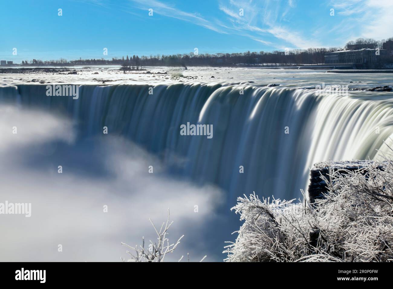 Panoramic view over the Niagara Falls, ON, Canada during winter with smooth slow shutter speed water flow from the falls and white ice on the bushes Stock Photo