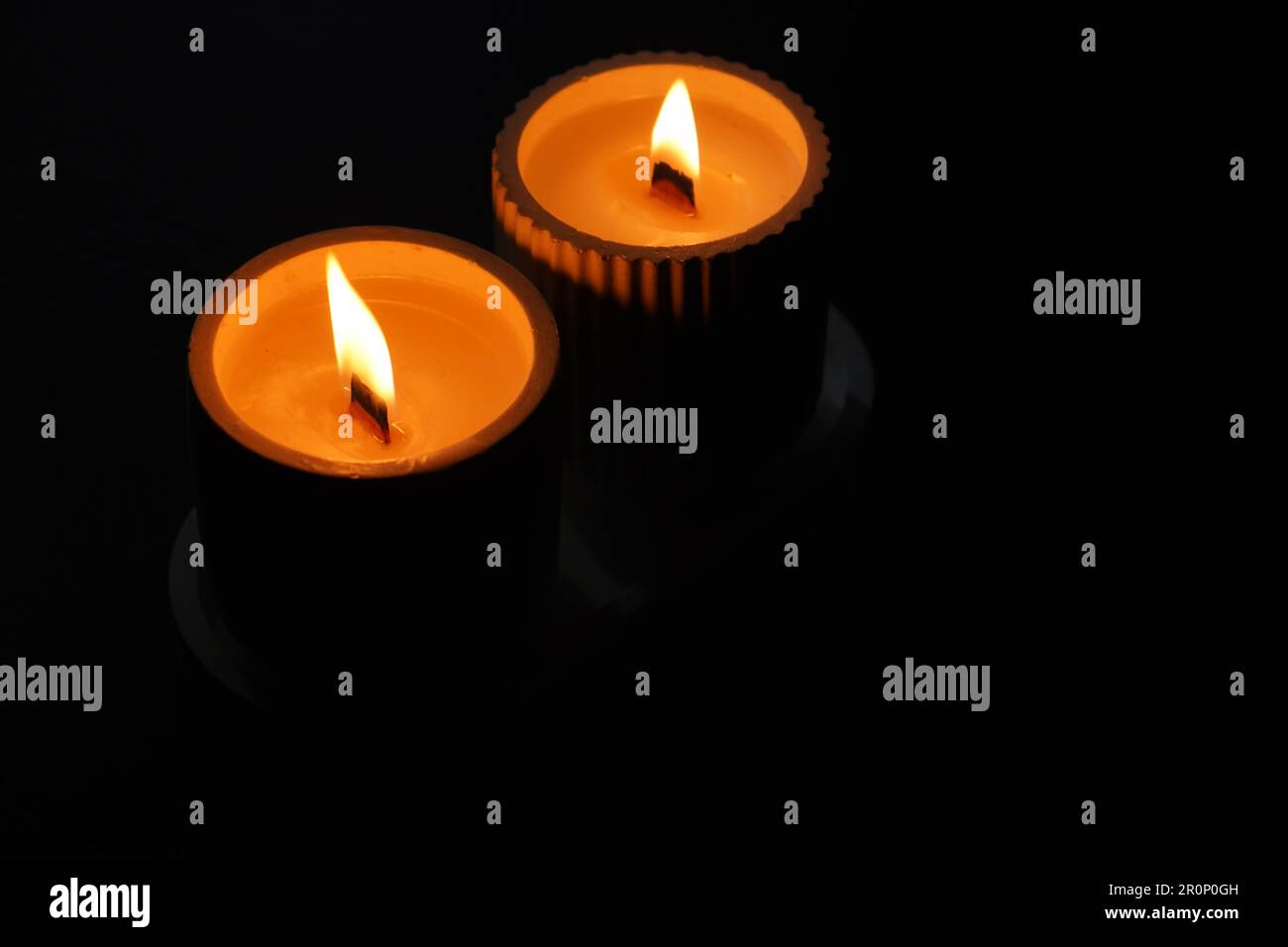 A set of lit white candles flickering in the dark on a black background with one candle in focus