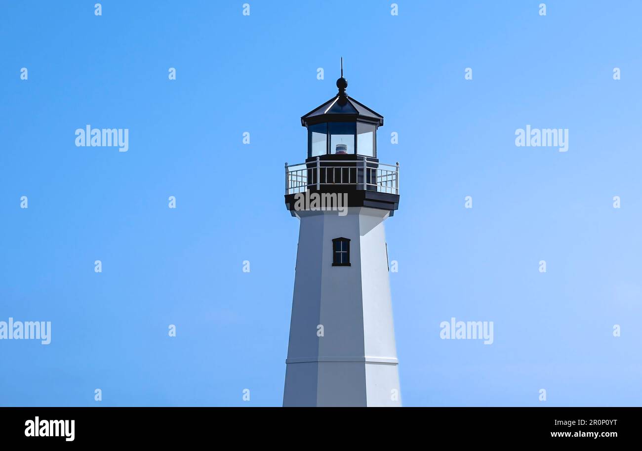 Lighthouse in daytime, centered against clear blue sky. Sky a bit