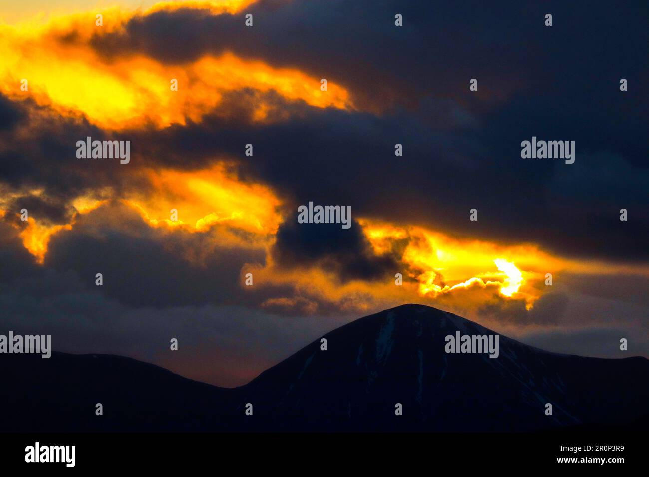 A dramatic orange and yellow sunset sky behind a range of majestic ...