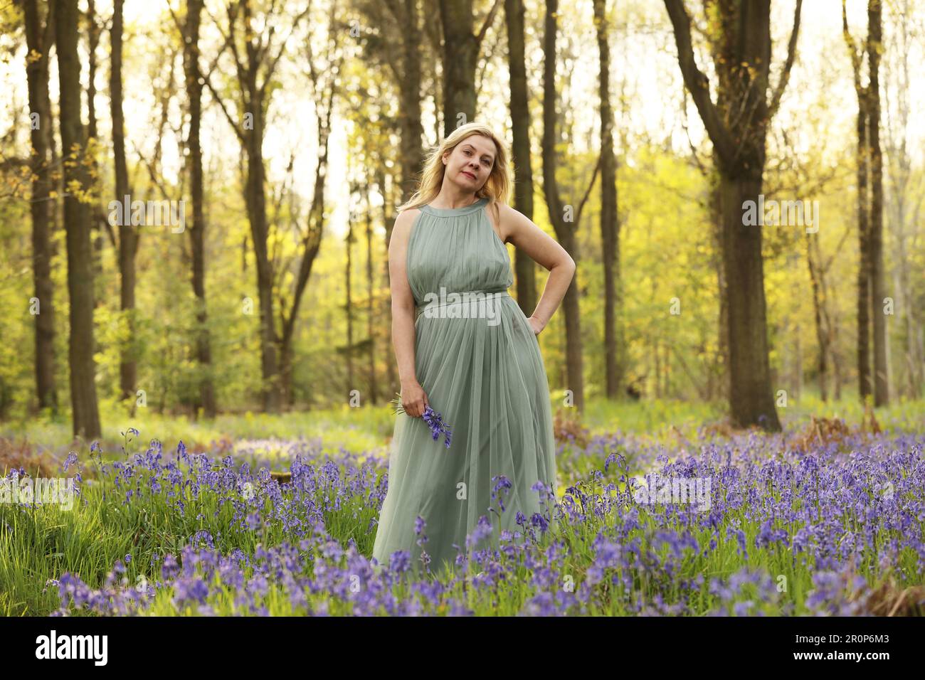 A woman standing in a bluebell wood wearing a long green dress Stock Photo