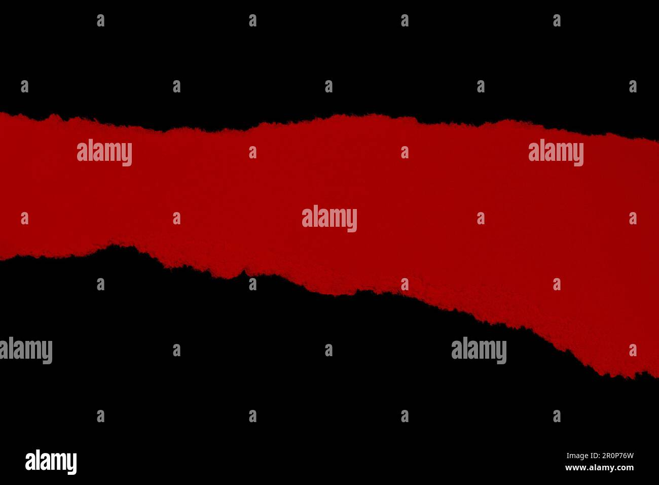 A red, torn cardboard piece isolated on a black background, illuminated ...