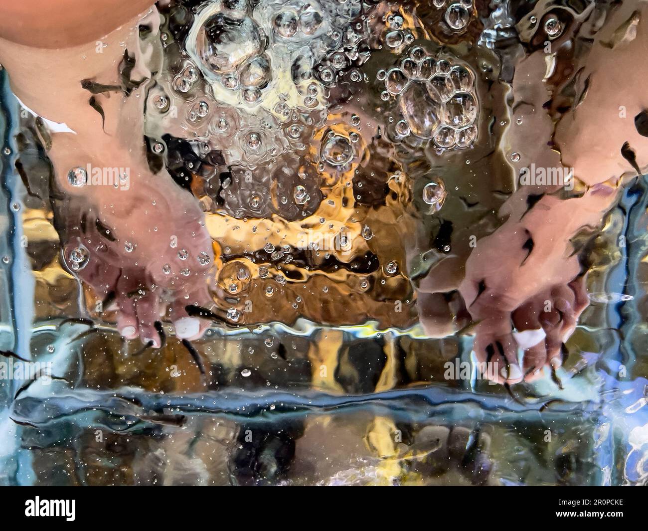 Young woman's feet immersed in a water tank where fish called 'Garra Rufa' clean and exfoliate the dead skin cells of the feet and massage them. Conce Stock Photo