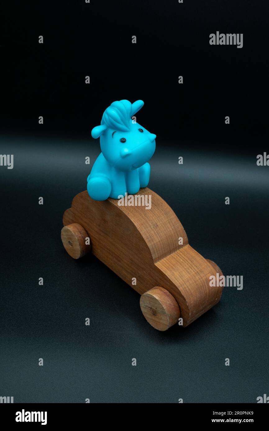 wooden toy car made from cherry wood with a blue toy animal riding on top, isolated on a black background Stock Photo