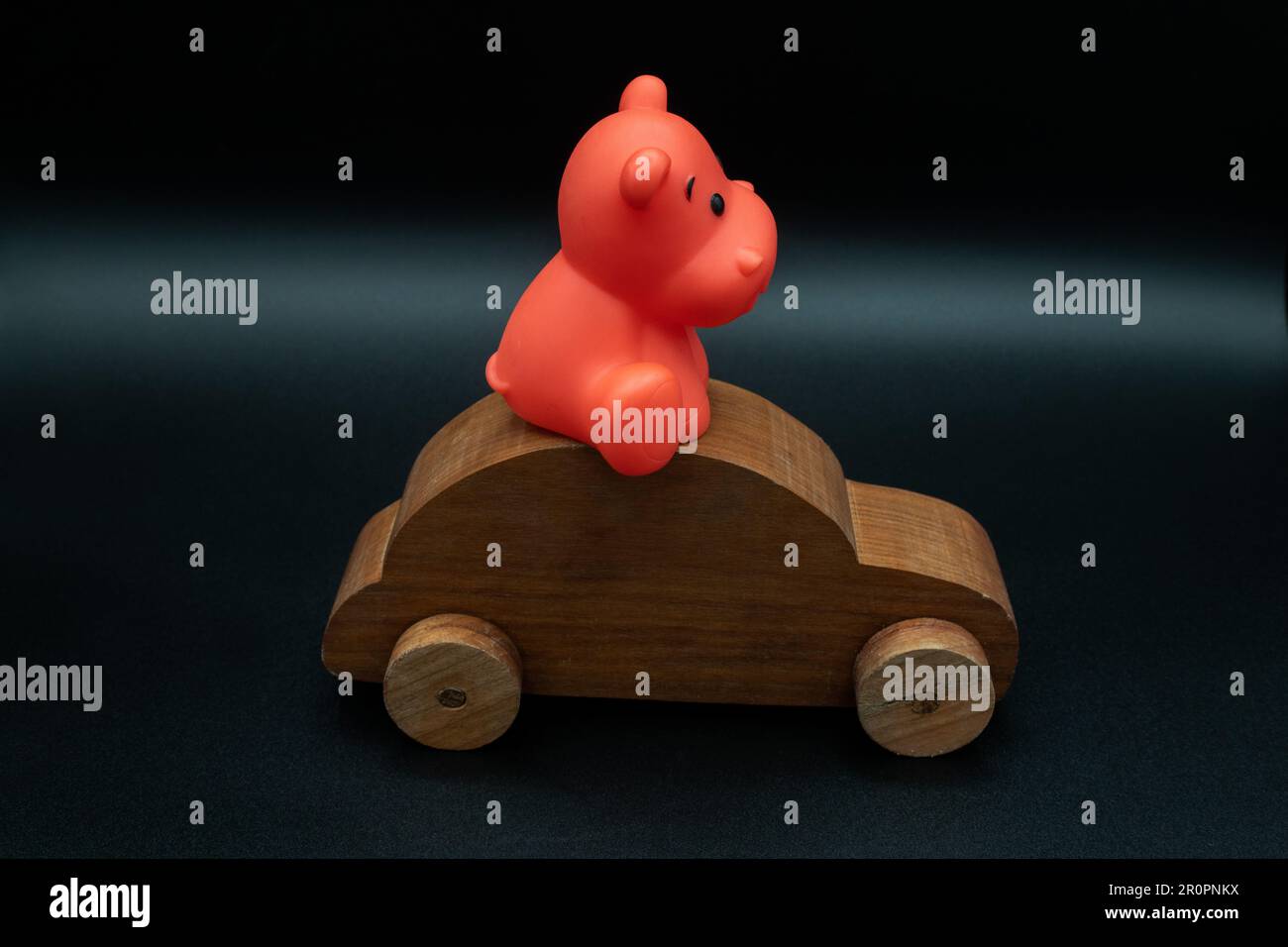 wooden toy car made from cherry wood with a toy animal riding on top, isolated on a black background, side view, profile, concept, driving, parking Stock Photo