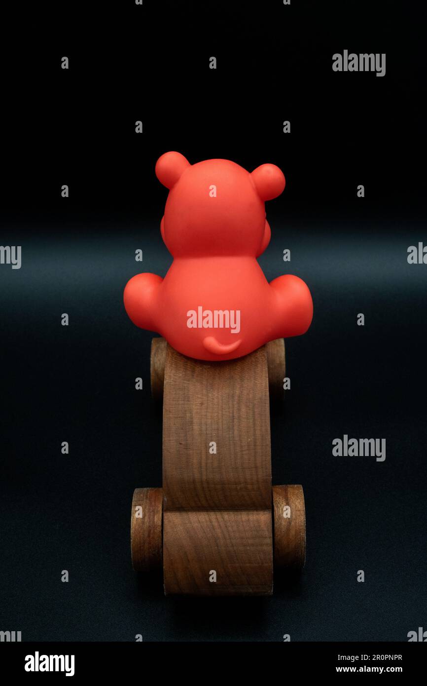 red toy animal riding on top wooden toy car going away, wooden toy car made from cherry wood, isolated on a black background, back view, back of car, Stock Photo
