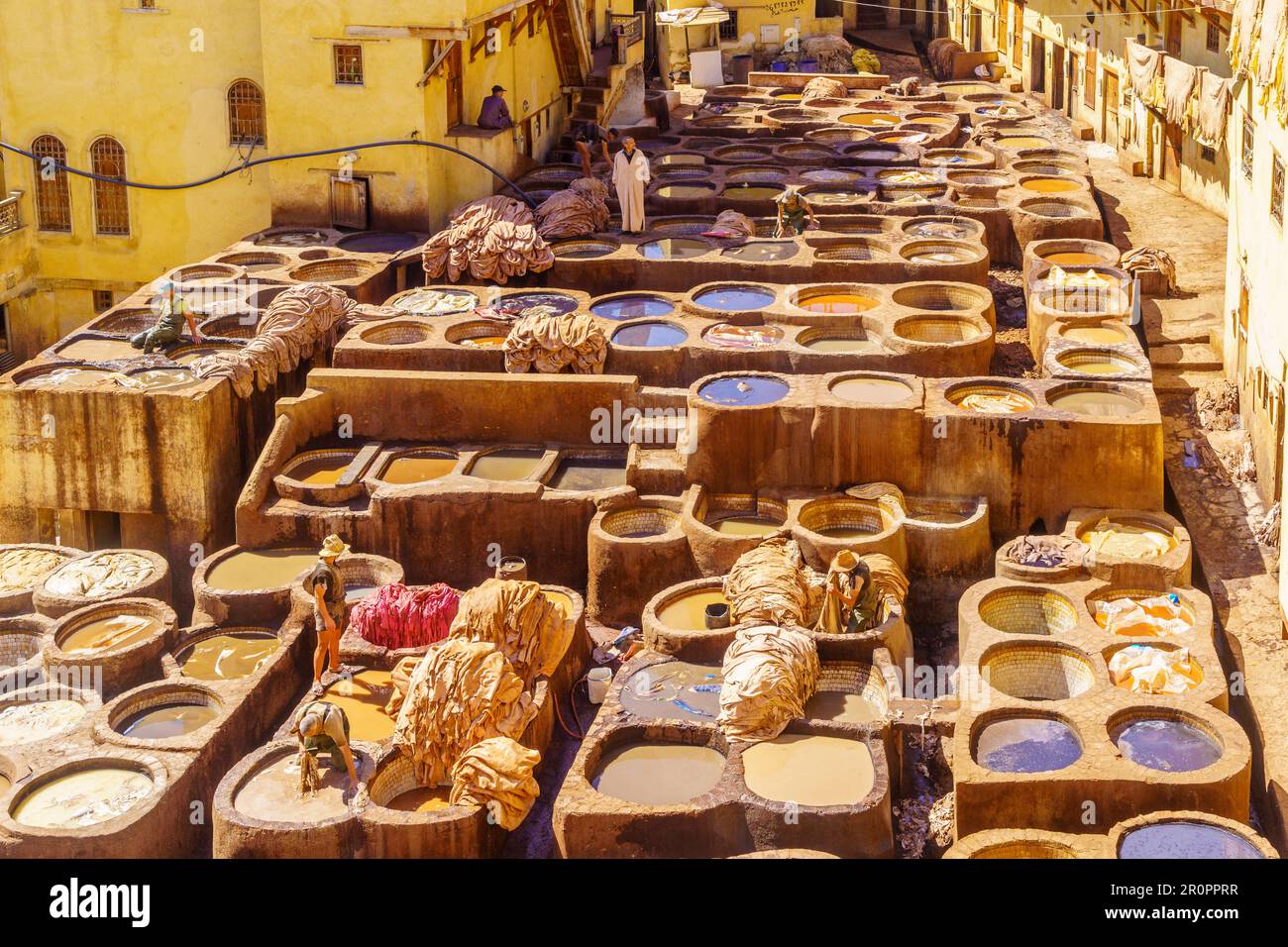 Fes, Morocco - March 31, 2023: View of the leather tannery with stone vats filled with various colors, and workers. Fes, Morocco Stock Photo