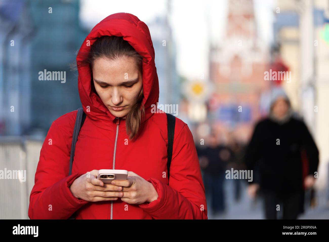 Girl in red coat walking down a street with smartphone. Using mobile phone in spring city Stock Photo
