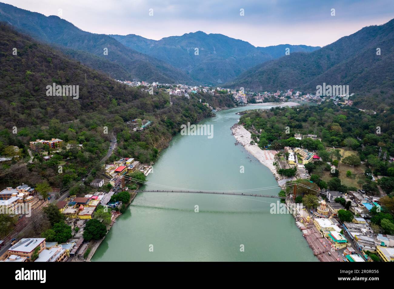 aerial drone shot of blue water of river ganga stretching into distance with himalayas with ram setu suspension bridge and temples on the banks of the Stock Photo