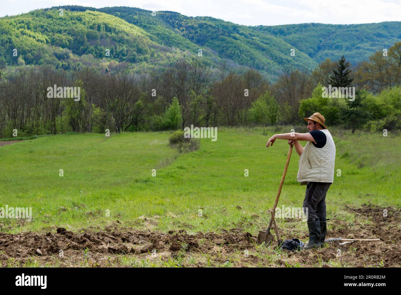 Farmer is standing leaning on his shovel and looking at the field he ...